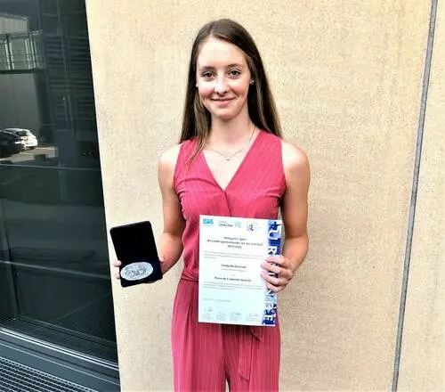 Junge Frau im roten Kleid hält eine Urkunde und ein Etui mit Medaille