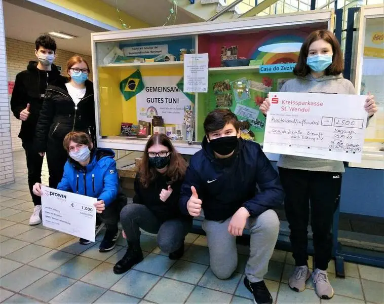 Schülergruppe mit Masken vor einer Vitrine, einige halten Urkunden oder Schecks