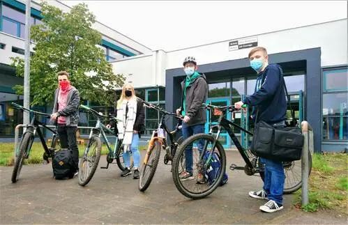 Erwachsene stehen mit ihren Fahrrädern auf dem Gelände vor einem Schulgebäude