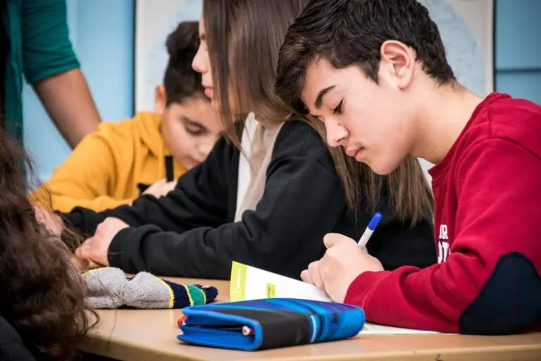 Schülerinnen und Schüler arbeiten an einem Tisch im Klassenraum und schreiben in Hefte