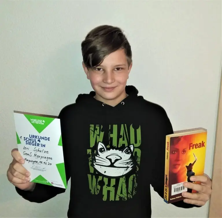 Junge im schwarzen Kapuzenpullover hält lächelnd zwei Bücher in die Kamera