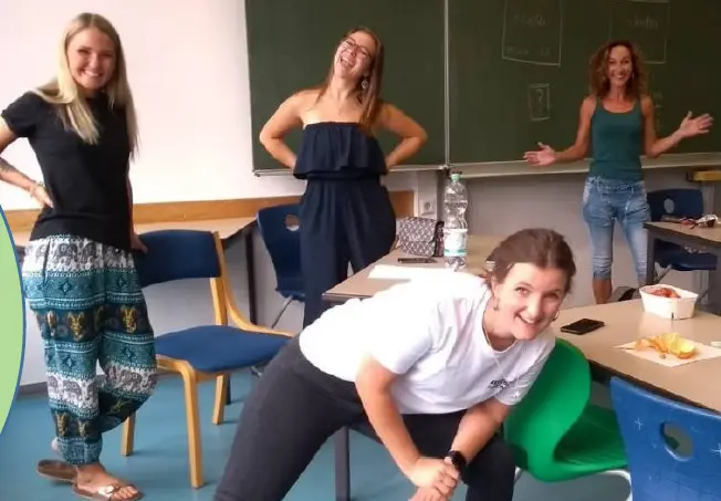 Junge Frauen posieren gut gelaunt in einem Klassenraum vor einer Tafel