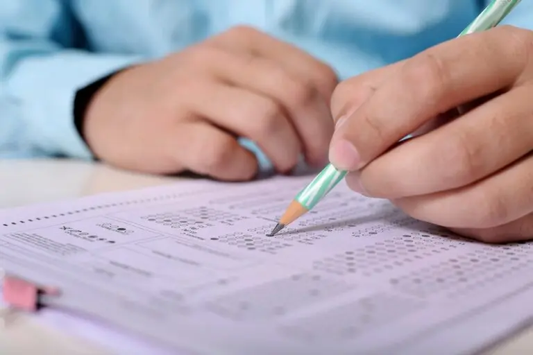 Nahaufnahme einer Hand, die mit Bleistift einen Prüfungsbogen ausfüllt