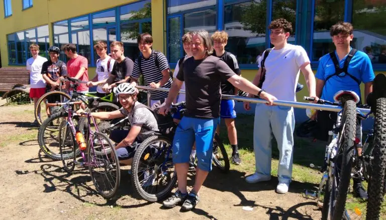 Jugendliche stehen mit ihren Fahrrädern auf einer Wiese vor dem Schulgebäude
