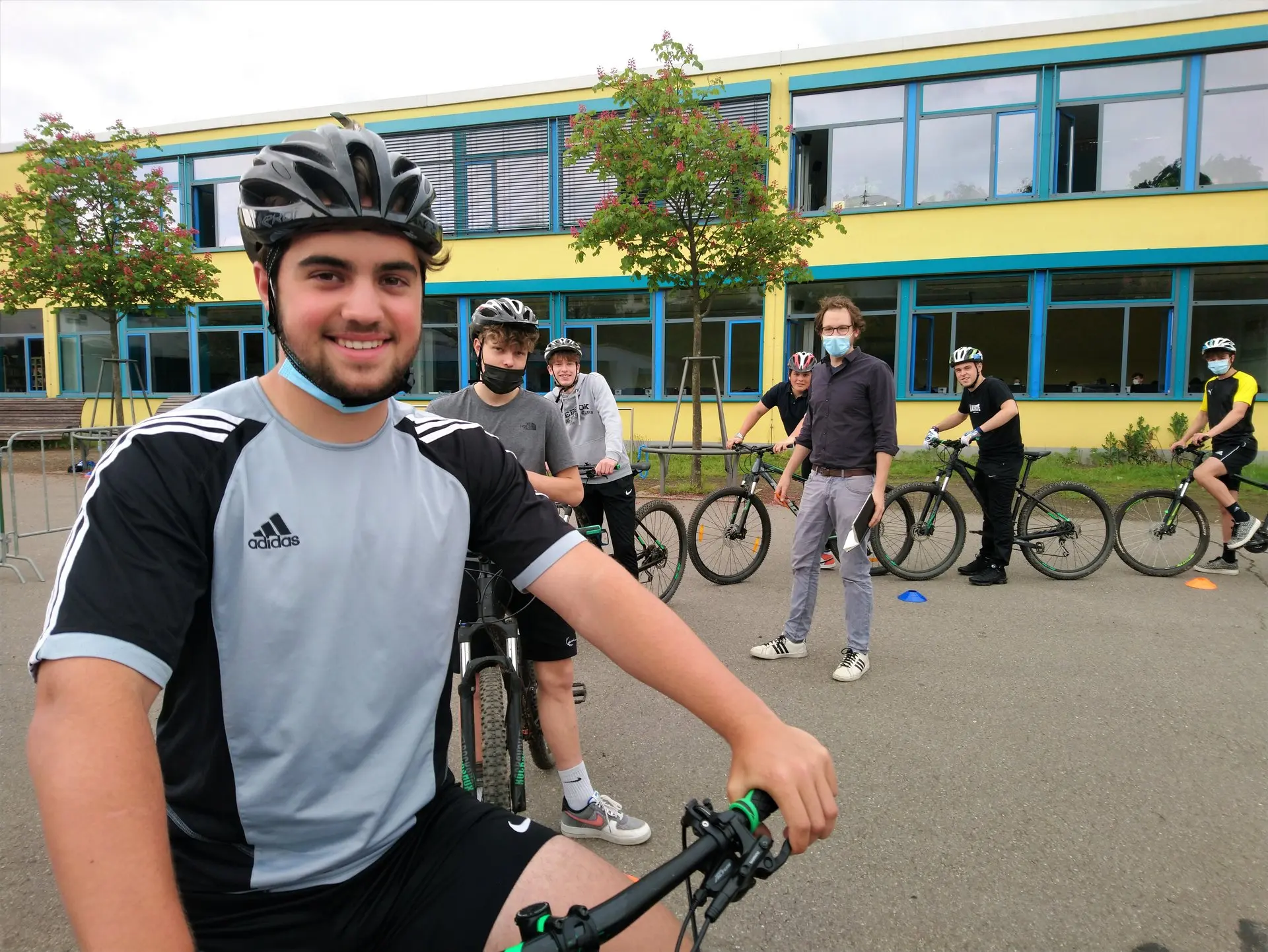 Schüler mit Fahrradhelm auf dem Fahrrad, im Hintergrund weitere Radfahrer auf dem Schulhof