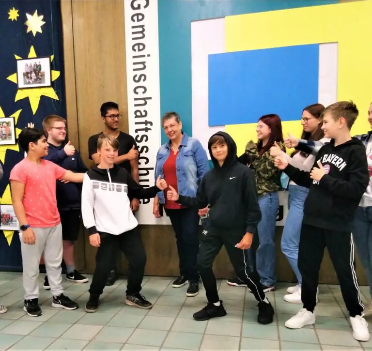 Gruppe von Schülerinnen und Schülern und eine Frau posieren ausgelassen vor einer bunten Wand