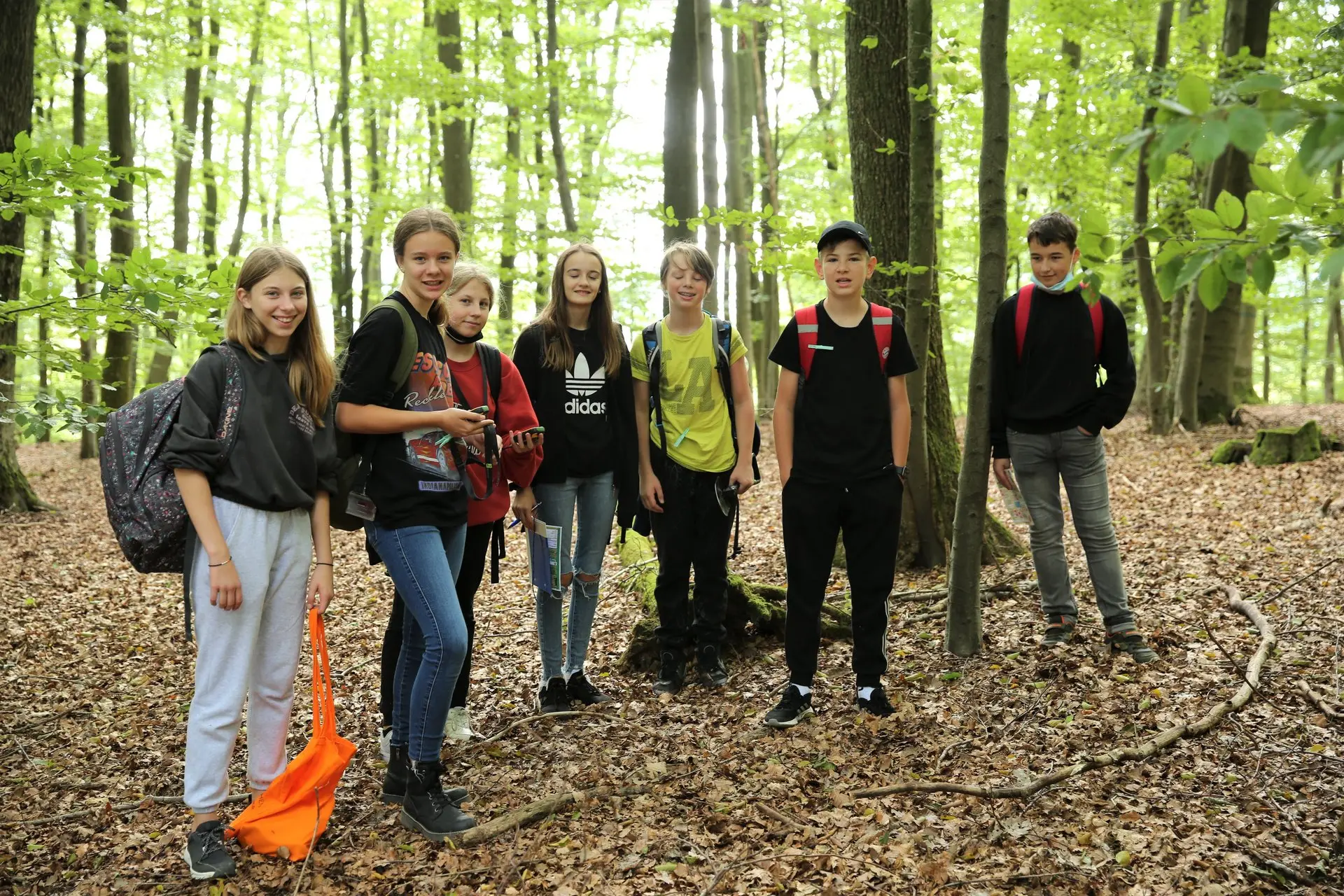 Gruppe von Jugendlichen steht auf einem Waldweg zwischen hohen Buchen
