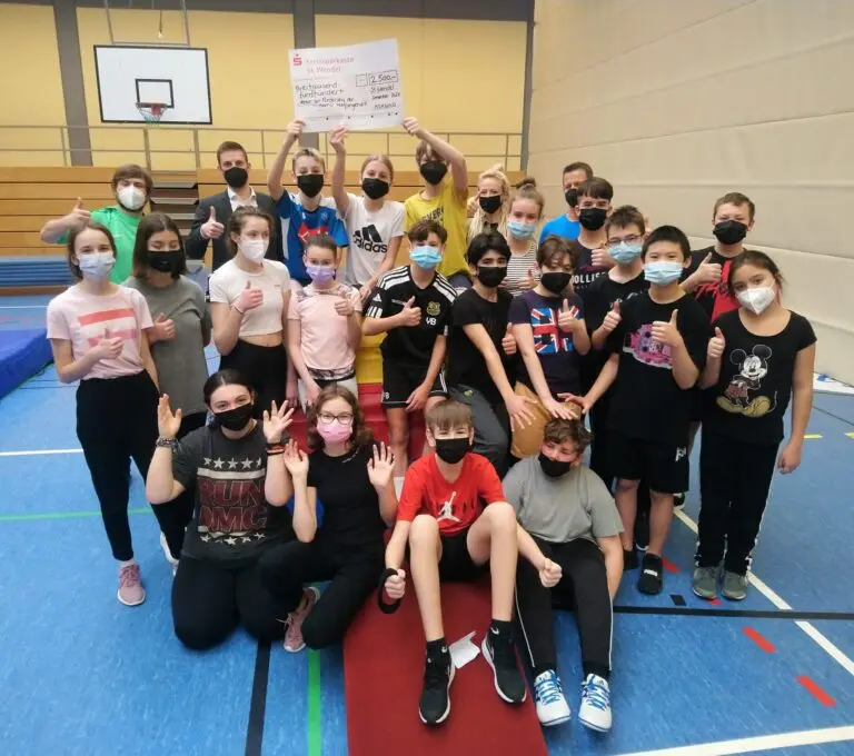 Schülergruppe mit Masken in der Turnhalle bei der Übergabe neuer Sportgeräte