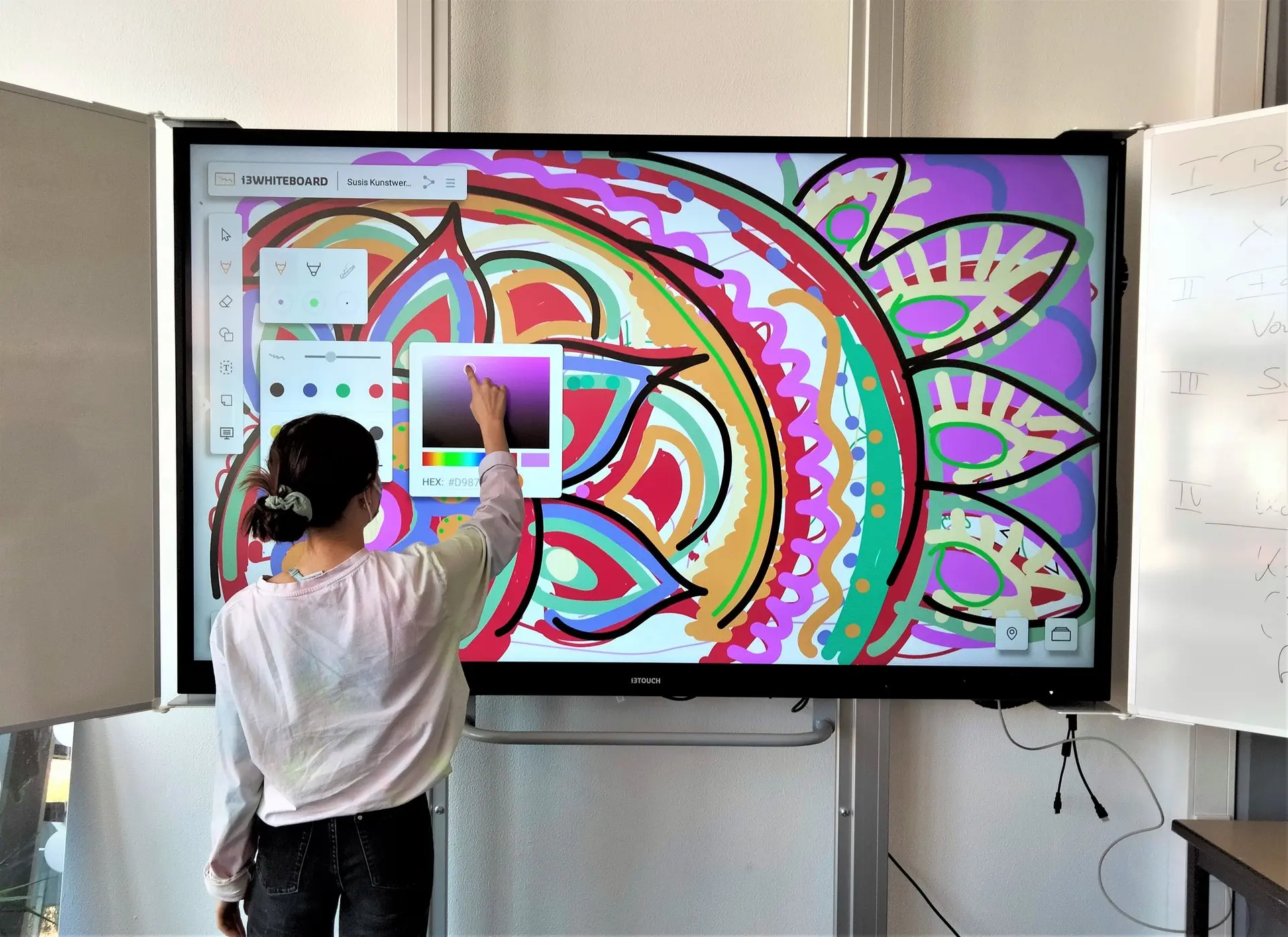 Schülerin bedient eine große interaktive Tafel mit einem bunten Mandala-Motiv