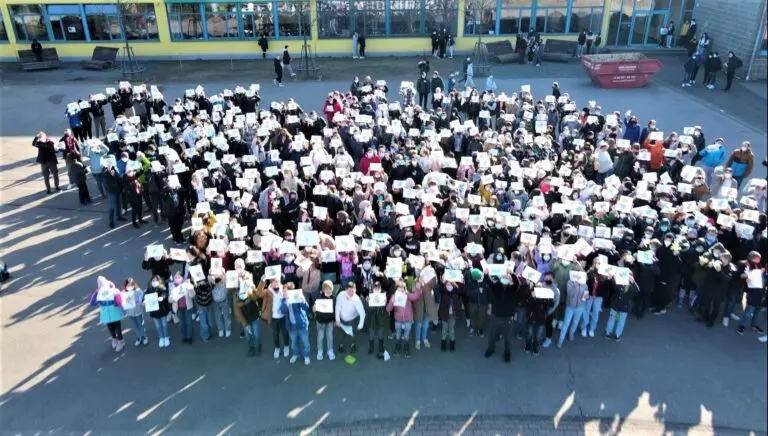 Luftaufnahme: viele Schülerinnen und Schüler bilden auf dem Schulhof eine Figur als Friedenszeichen