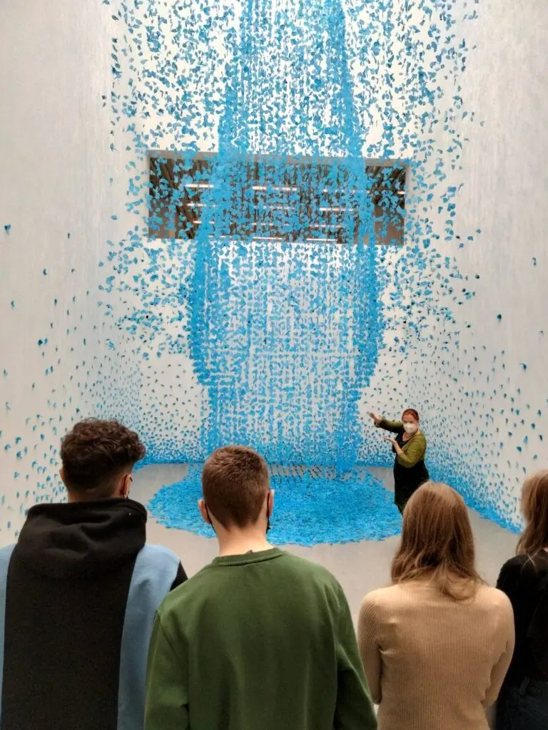 Jugendliche betrachten eine Installation aus blauen hängenden Elementen in einem Museum