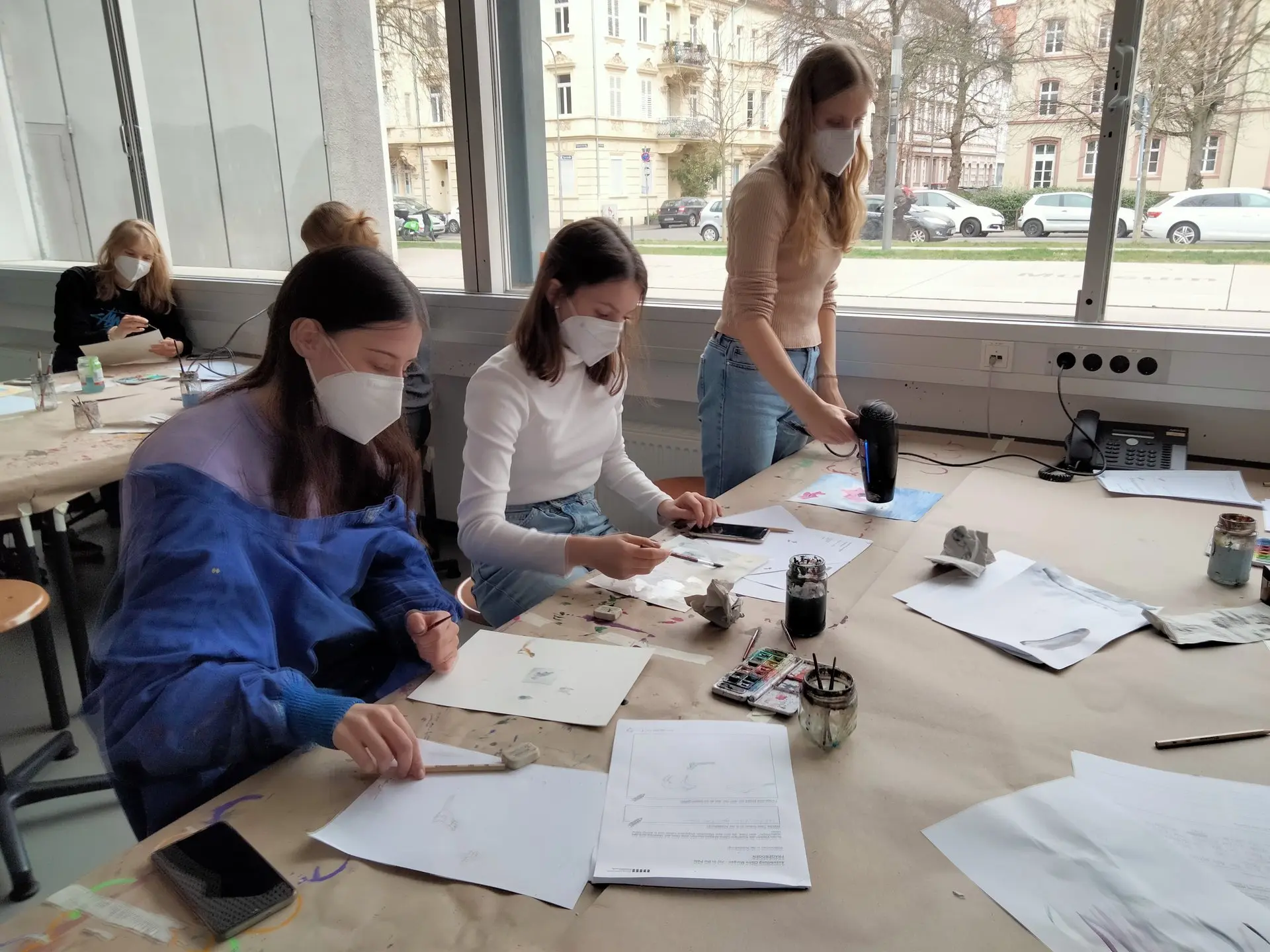Schülerinnen arbeiten mit Masken an Tischen in einem Museums-Werkraum an Zeichnungen