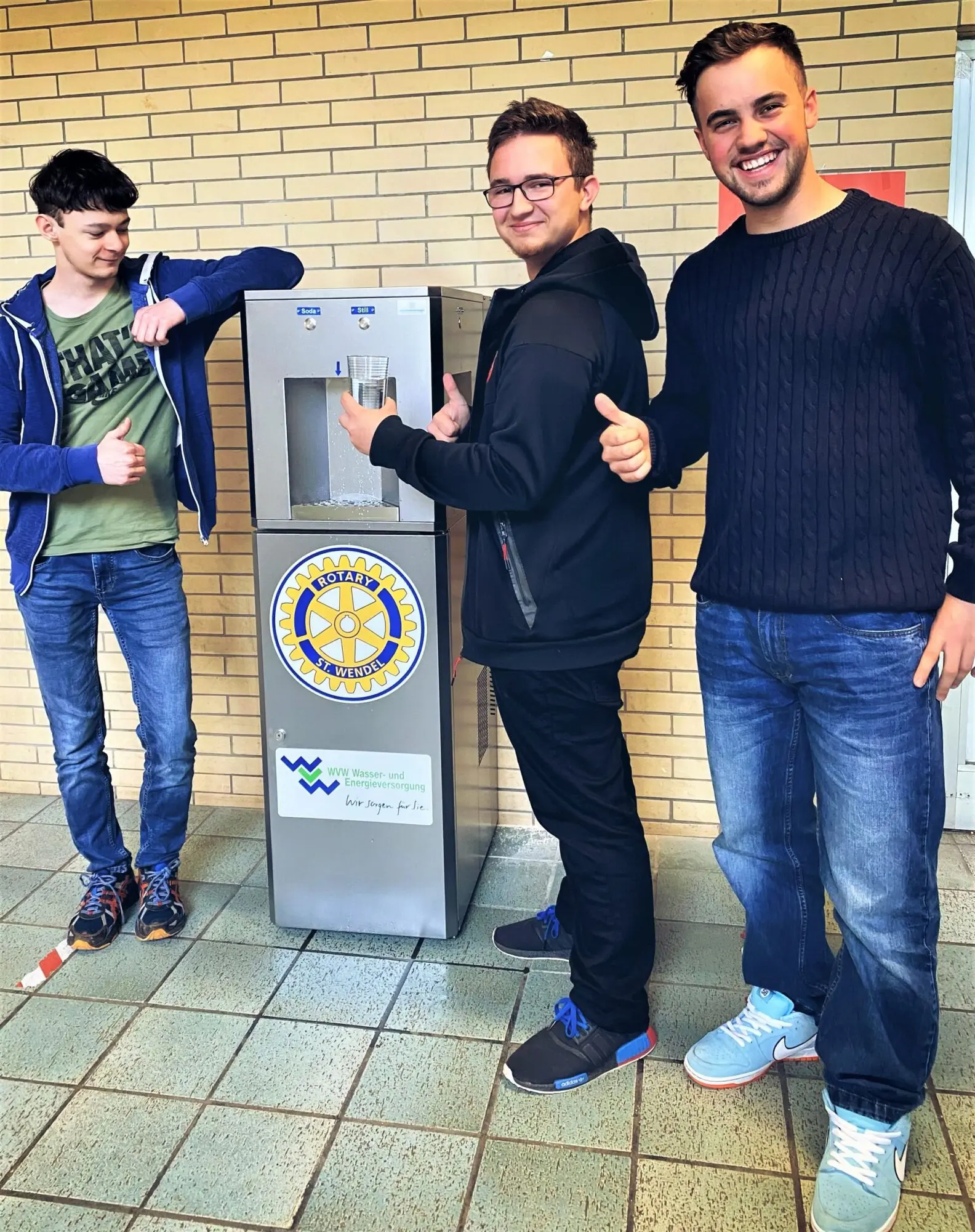 Zwei Schüler und ein Mann stehen neben einem Pfandflaschen-Rückgabeautomaten in der Schule