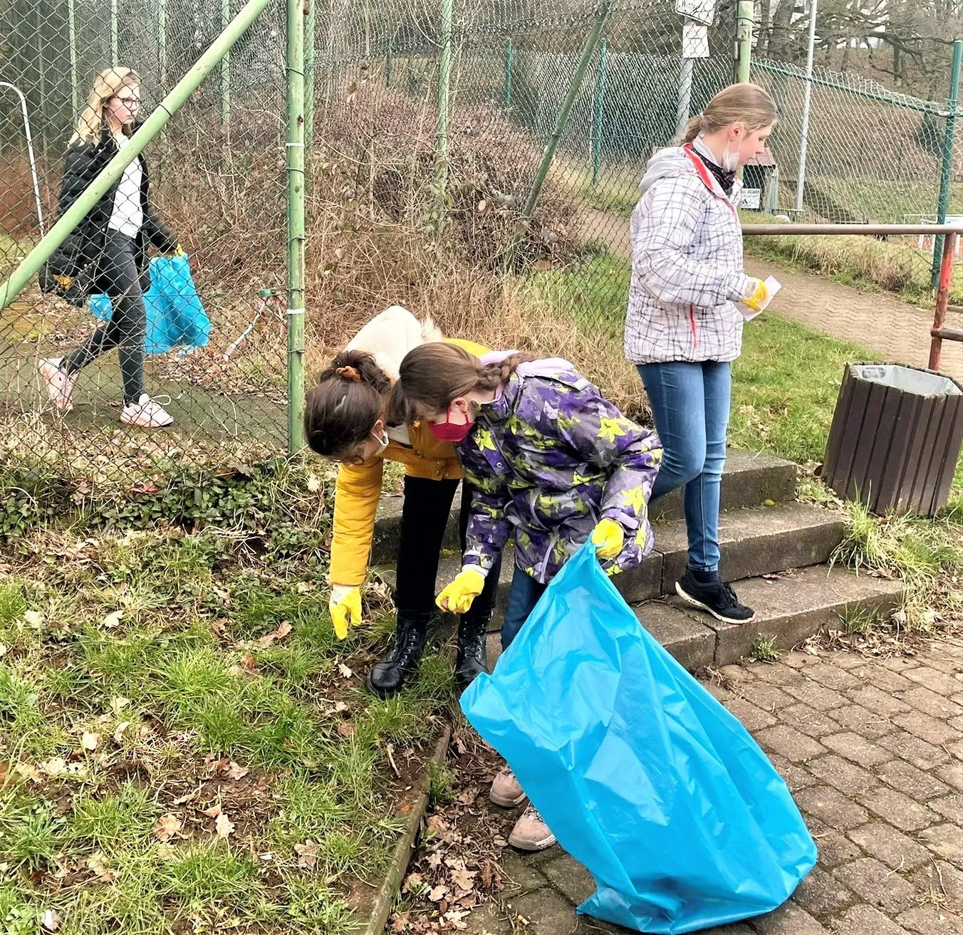 Schülerinnen und Schüler sammeln an einem Hang Müll in blaue Säcke