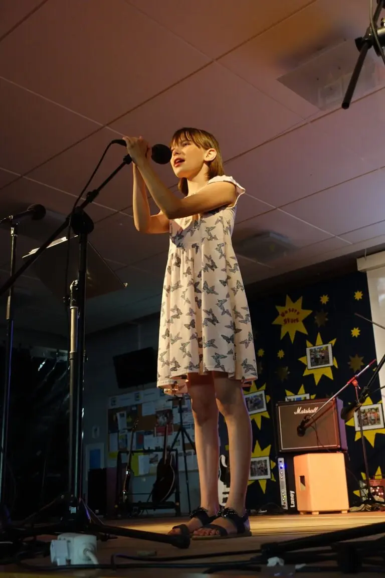 Sängerin im geblümten Kleid singt am Mikrofon auf einer Bühne beim Schulkonzert