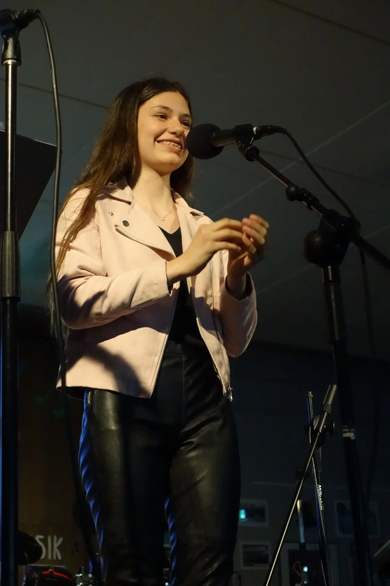 Sängerin in heller Jacke singt am Mikrofon vor dunklem Hintergrund