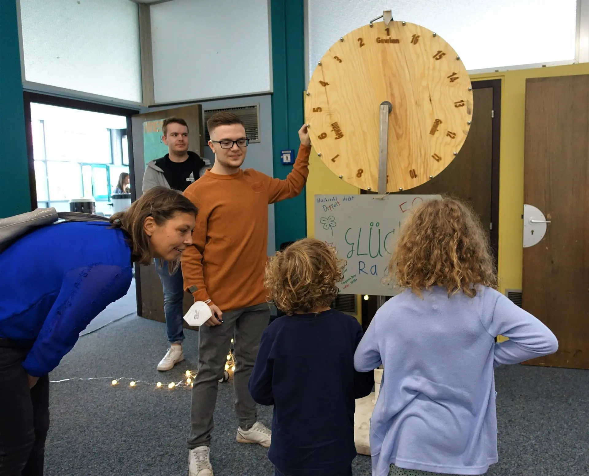 Kinder und Erwachsene vor einem großen Glücksrad aus Holz beim Schulfest