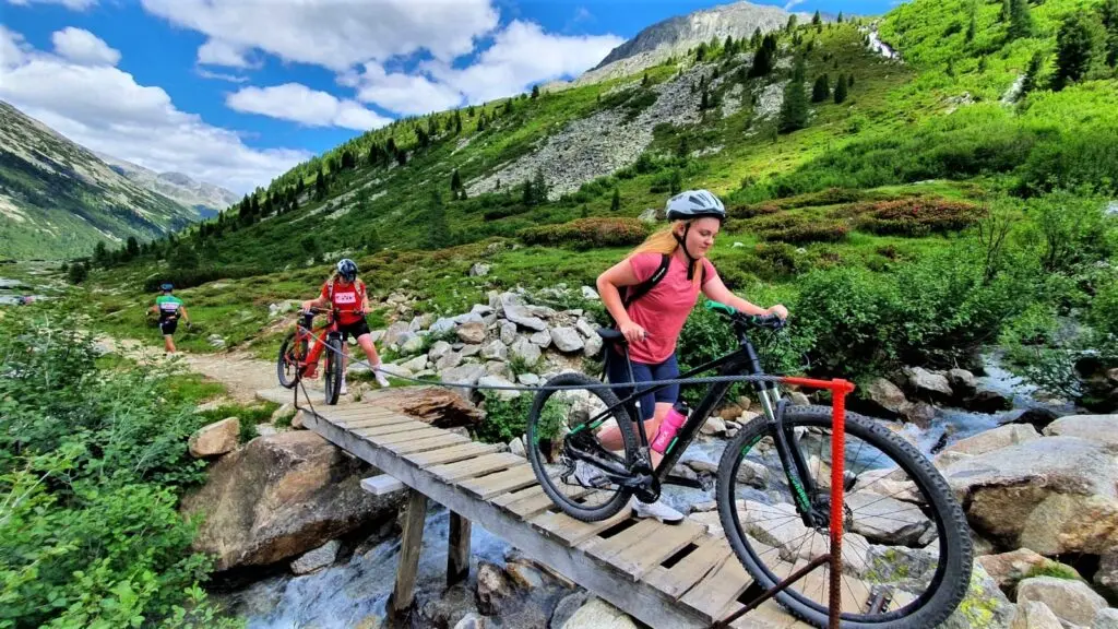 Mountainbikerin überquert eine Holzbrücke über einen Bach in grüner Berglandschaft