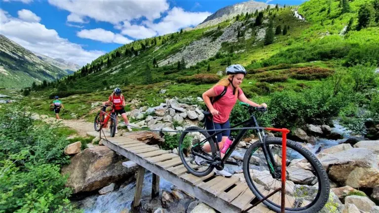 Mountainbikerin überquert eine Holzbrücke über einen Bach in grüner Berglandschaft