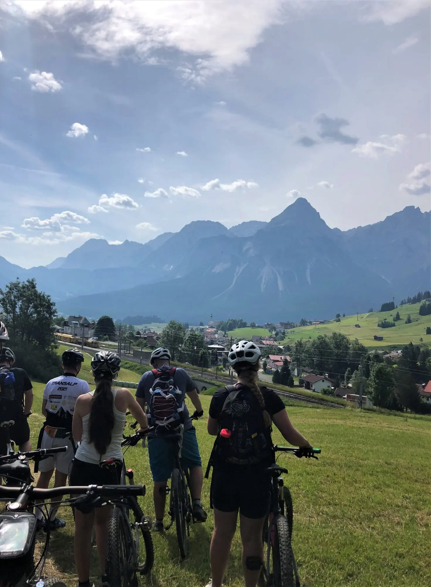 Mountainbiker mit ihren Rädern auf einer Wiese vor Alpengipfeln