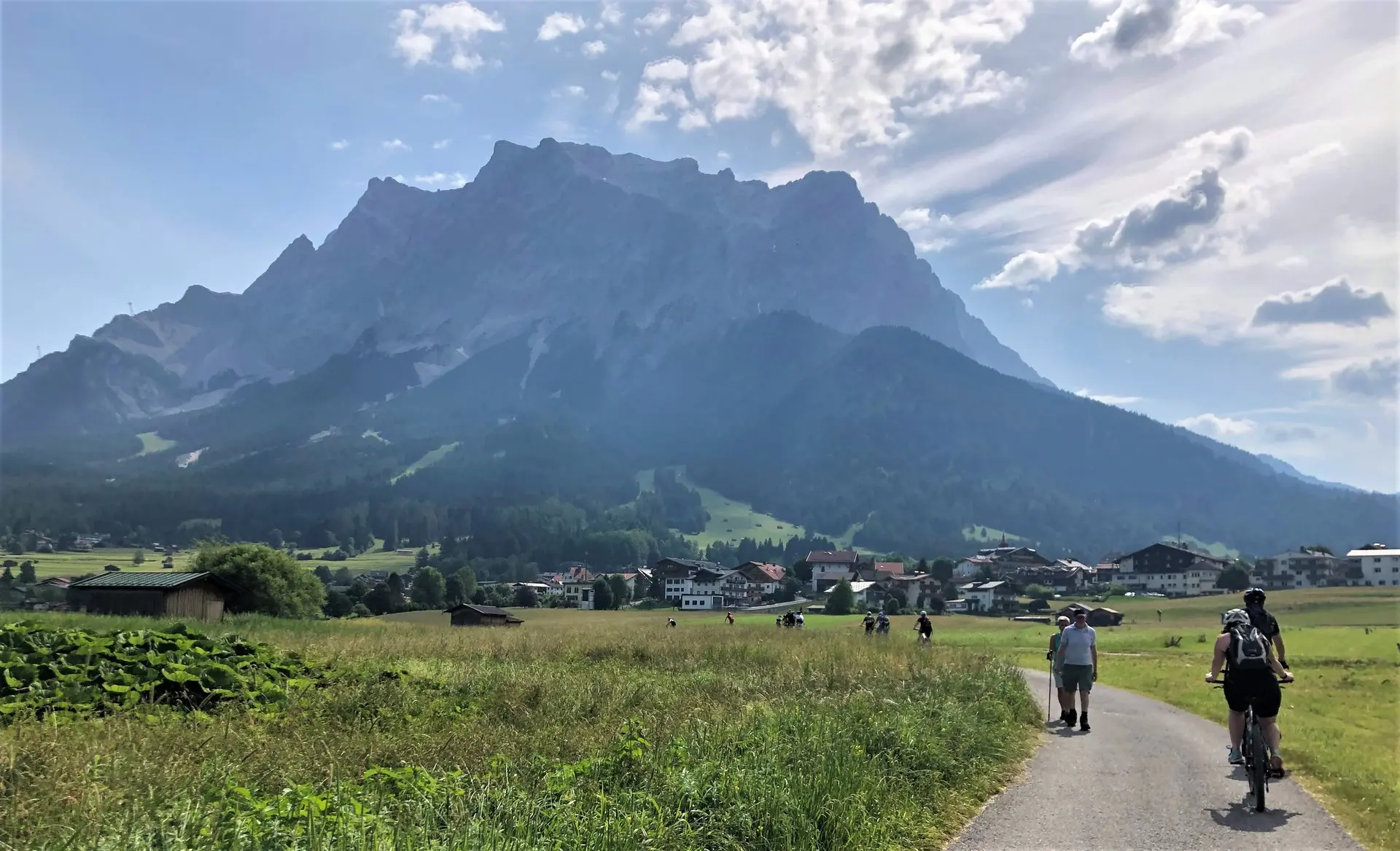 Radfahrer auf einem Weg durch eine Wiese vor einem mächtigen Felsmassiv