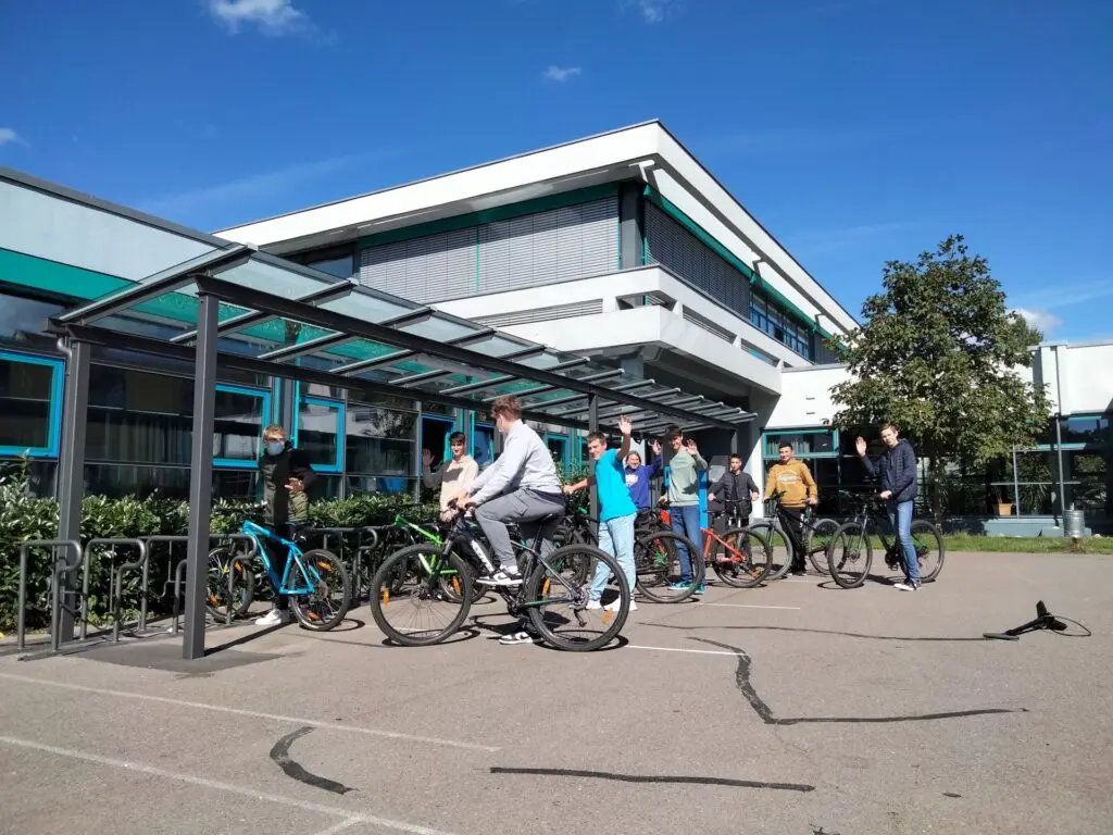 Schülerinnen und Schüler fahren auf dem Schulhof mit Fahrrädern vor dem Schulgebäude