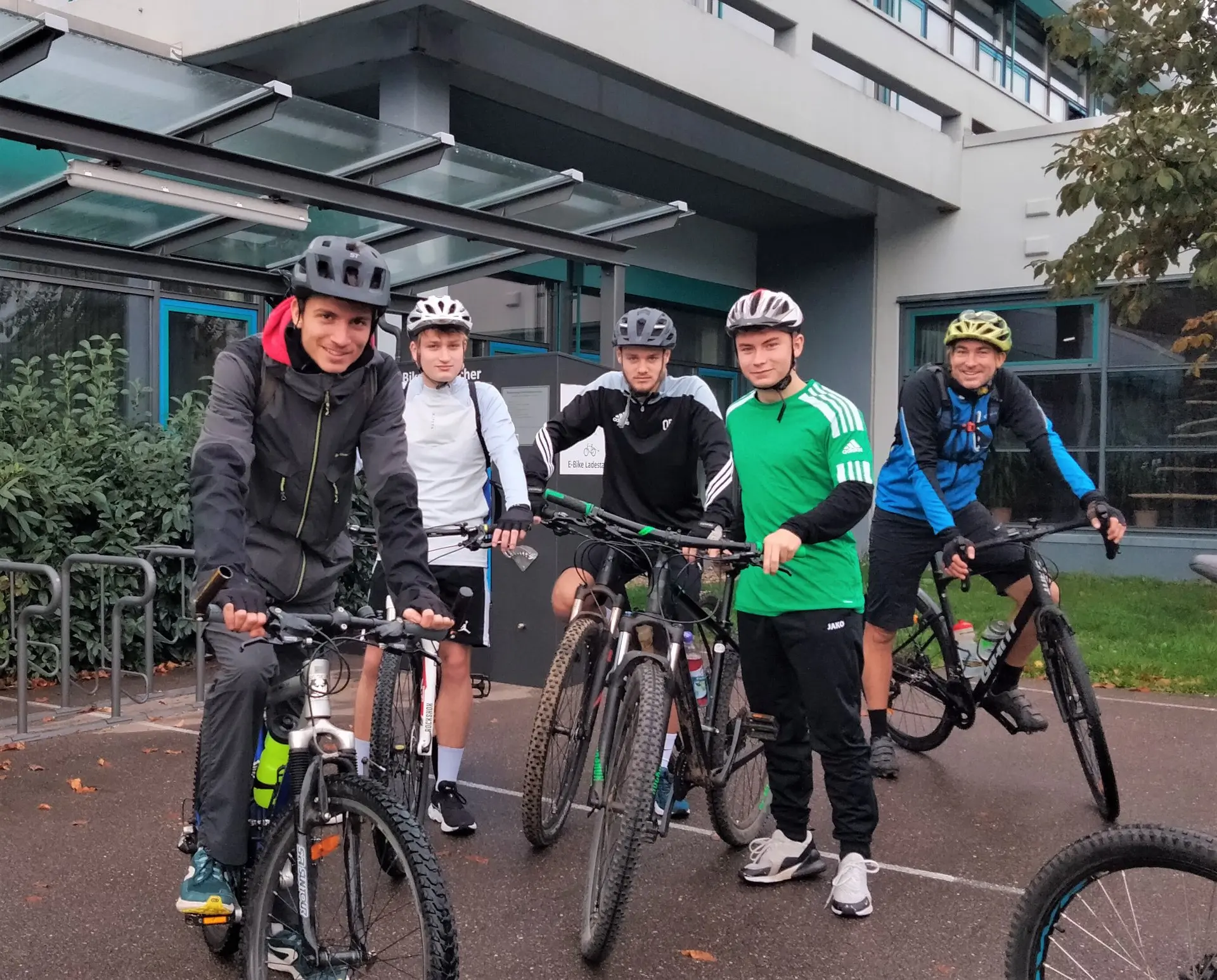 Gruppe Jugendlicher mit Helmen steht mit Fahrrädern vor der Schule