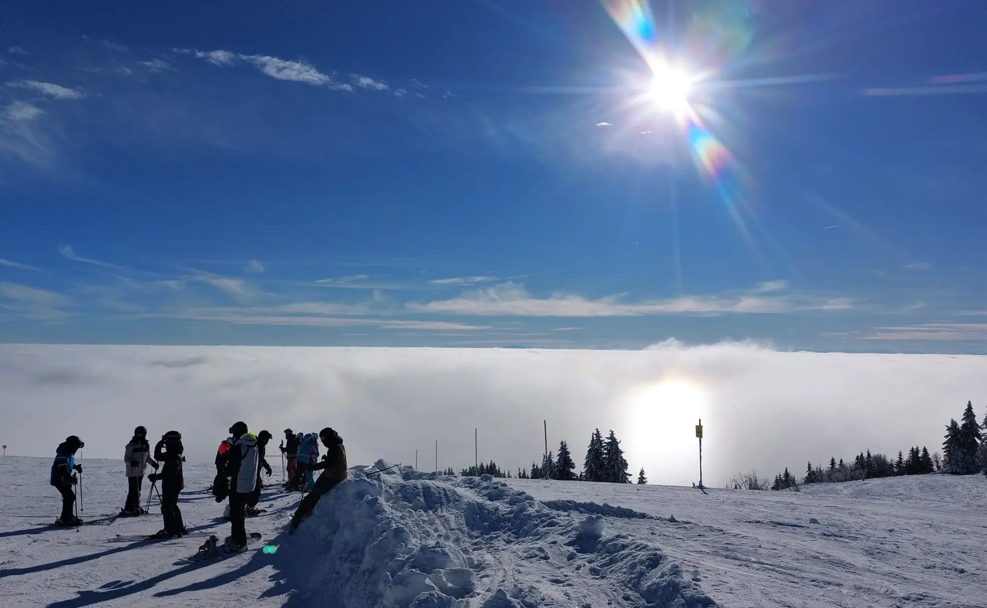 Personen stehen auf einem verschneiten Gipfel über einem Wolkenmeer im Gegenlicht