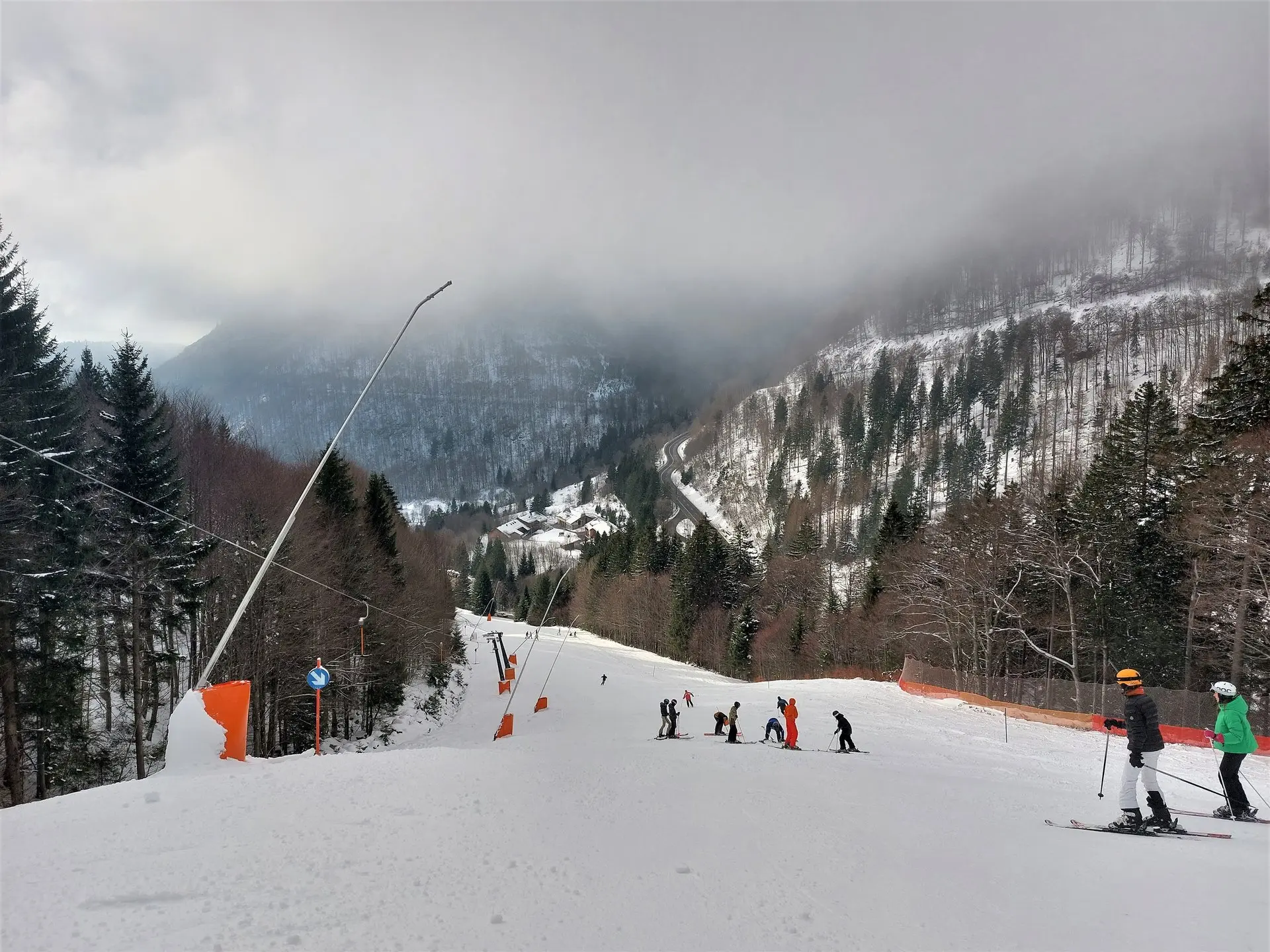 Skifahrer auf einer Piste zwischen verschneiten Tannenwäldern bei bewölktem Himmel