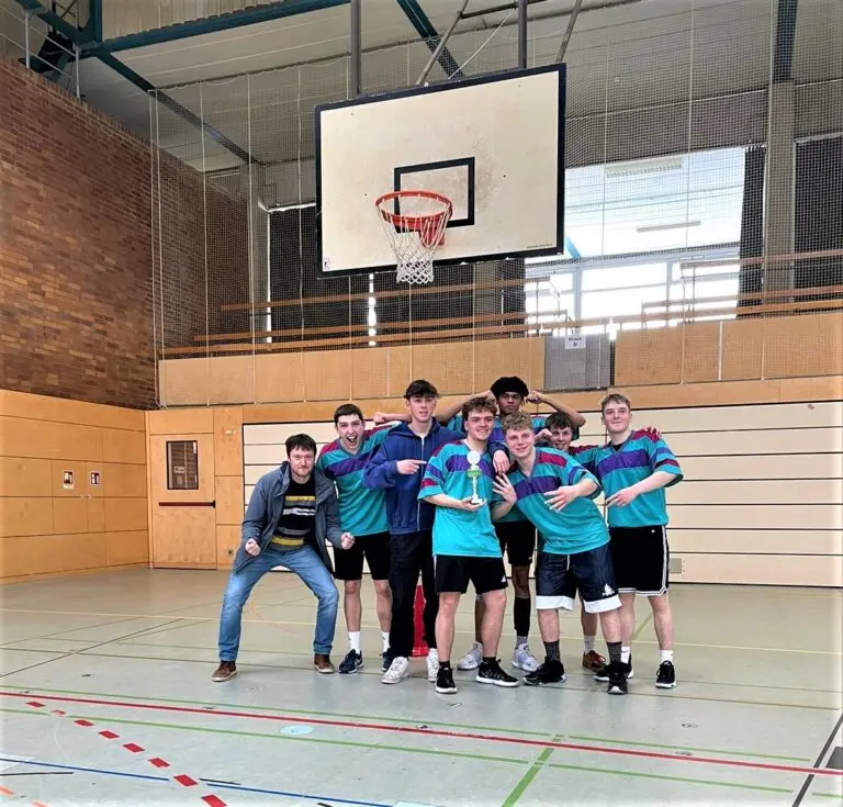 Schulmannschaft in türkisen Trikots jubelt in der Sporthalle unter dem Basketballkorb