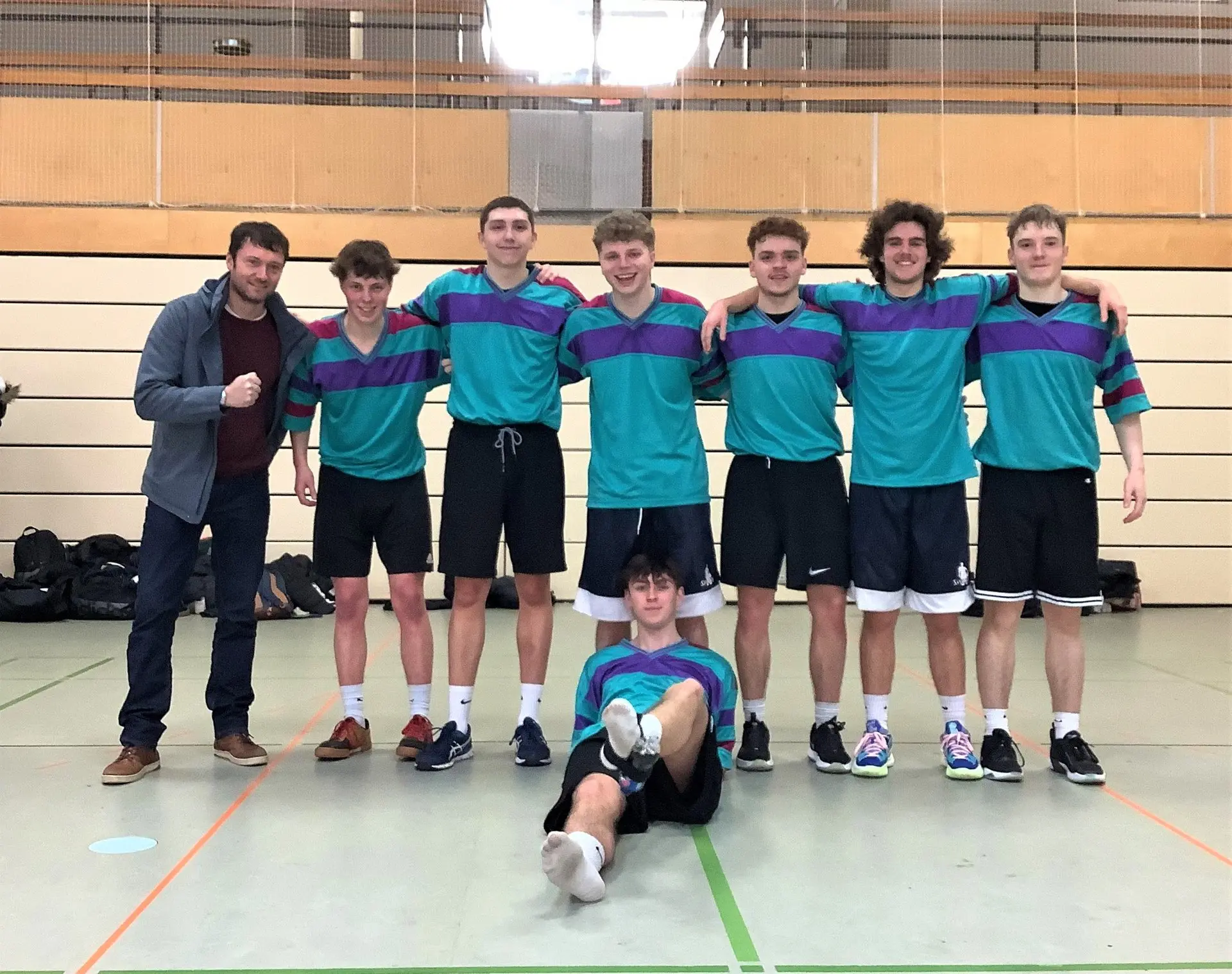 Volleyballmannschaft in türkisen Trikots mit Trainer in der Sporthalle