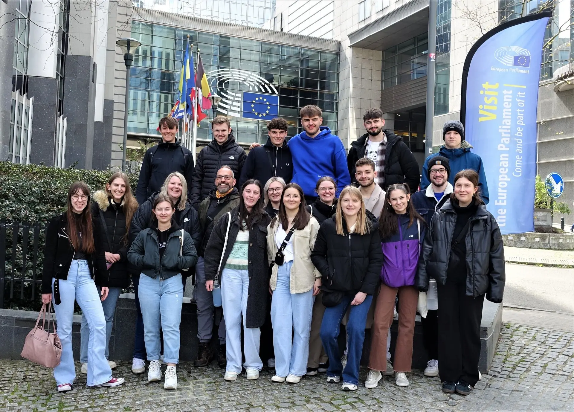 Gruppenbild der Schülergruppe vor einem modernen Gebäude mit Europaflaggen in Brüssel