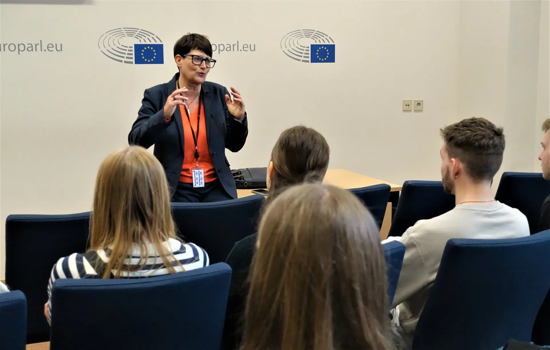 Rednerin spricht vor Schülerinnen und Schülern in einem Saal, an der Wand Logos der EU-Institution