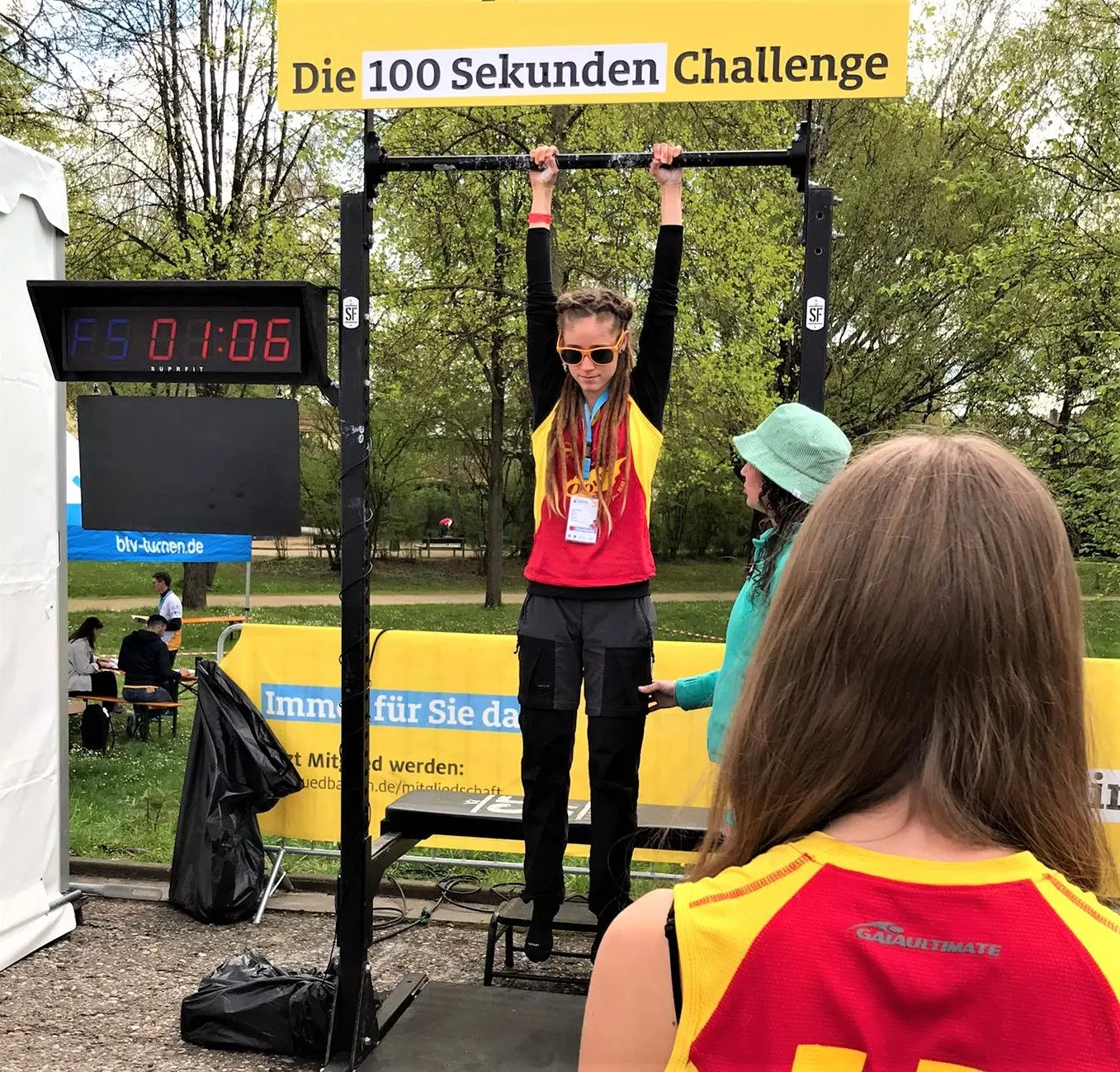 Schülerin hängt bei der „100 Sekunden Challenge“ an einer Klimmzugstange, daneben eine Zeitanzeige