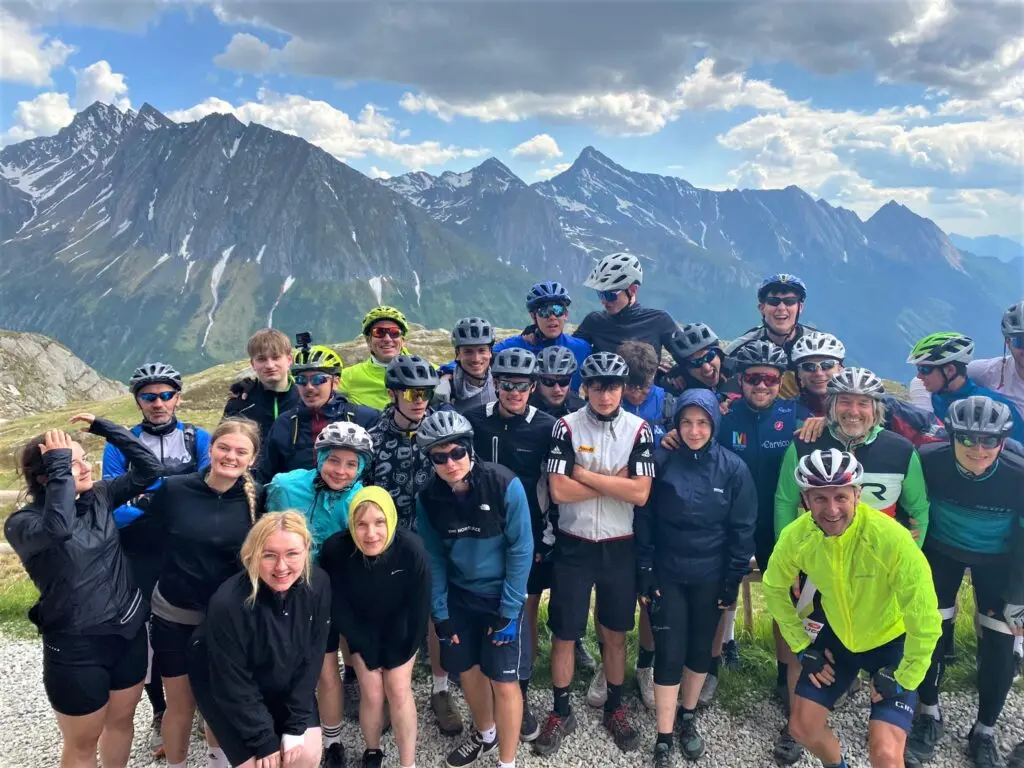 Gruppenbild der Radfahrerinnen und Radfahrer mit Helmen vor einer schneebedeckten Alpenkulisse