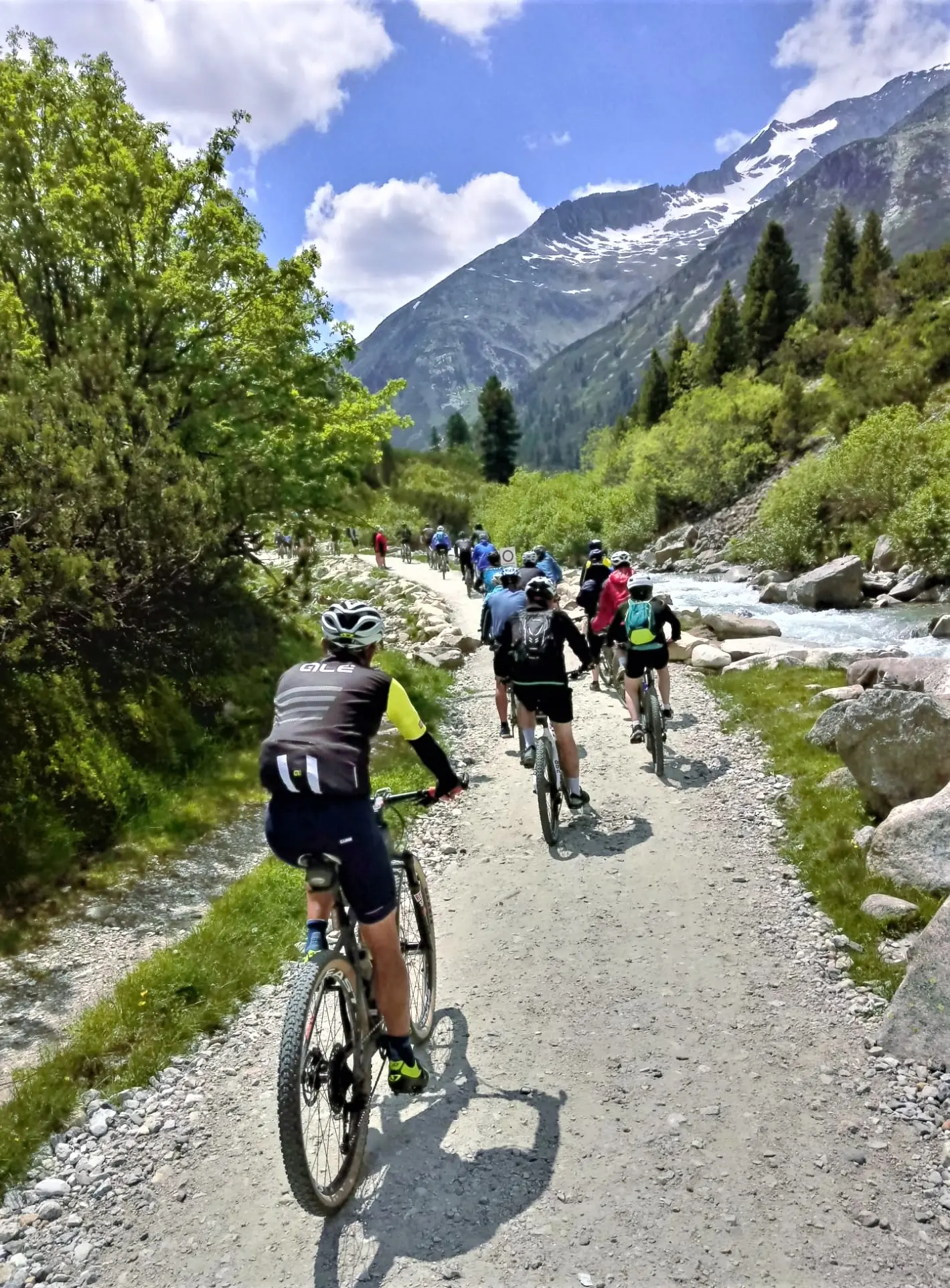Mountainbiker fahren auf einem Schotterweg neben einem Gebirgsbach durch ein Alpental