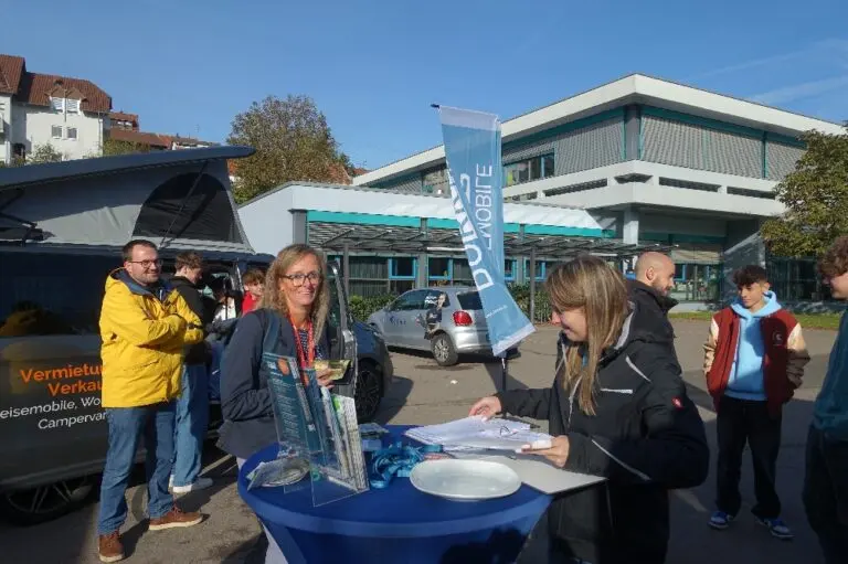 Menschen an einem Infostand mit Fahne vor dem Schulgebäude im Freien