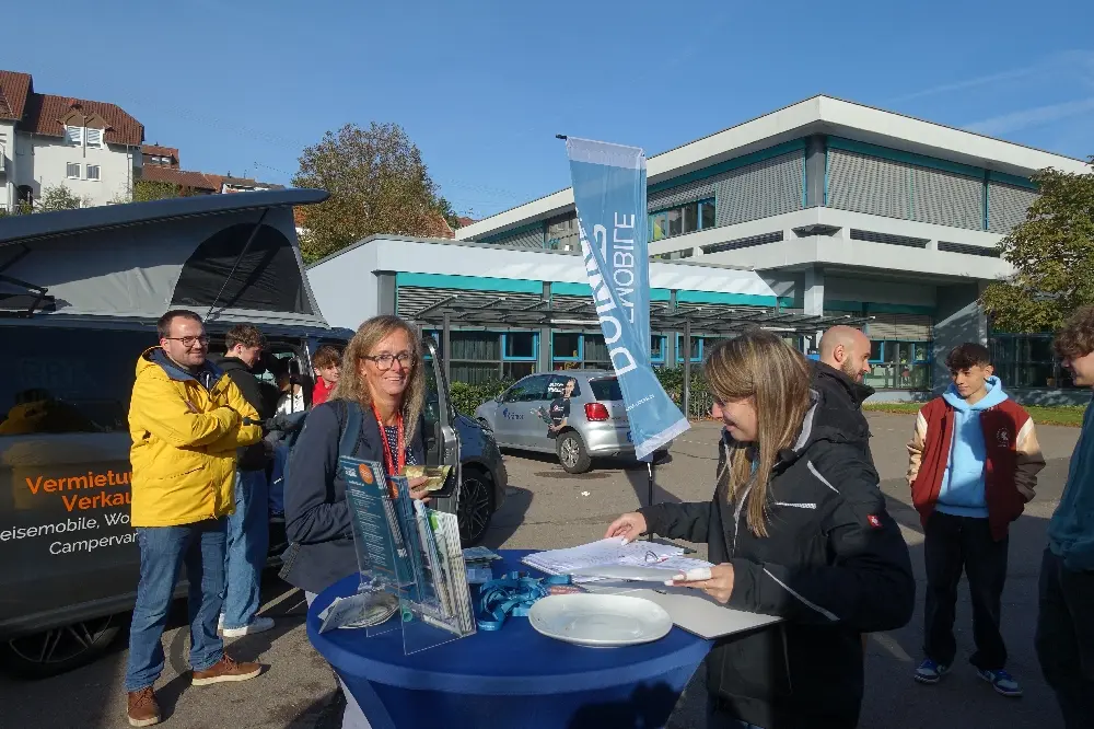 Menschen an einem Infostand mit Fahne vor dem Schulgebäude im Freien