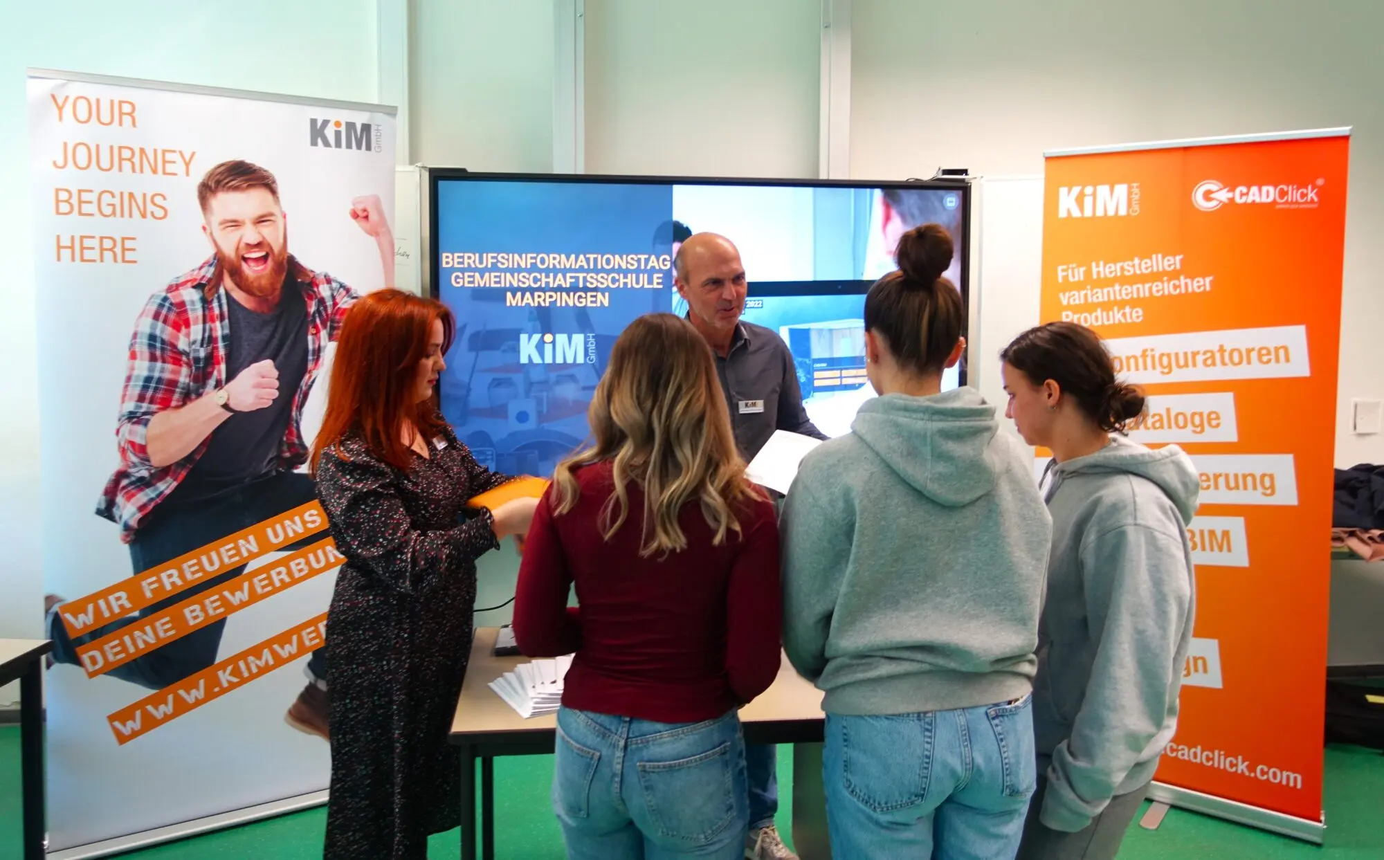 Schülerinnen informieren sich bei einem Firmenvertreter an einem Stand mit Rollups