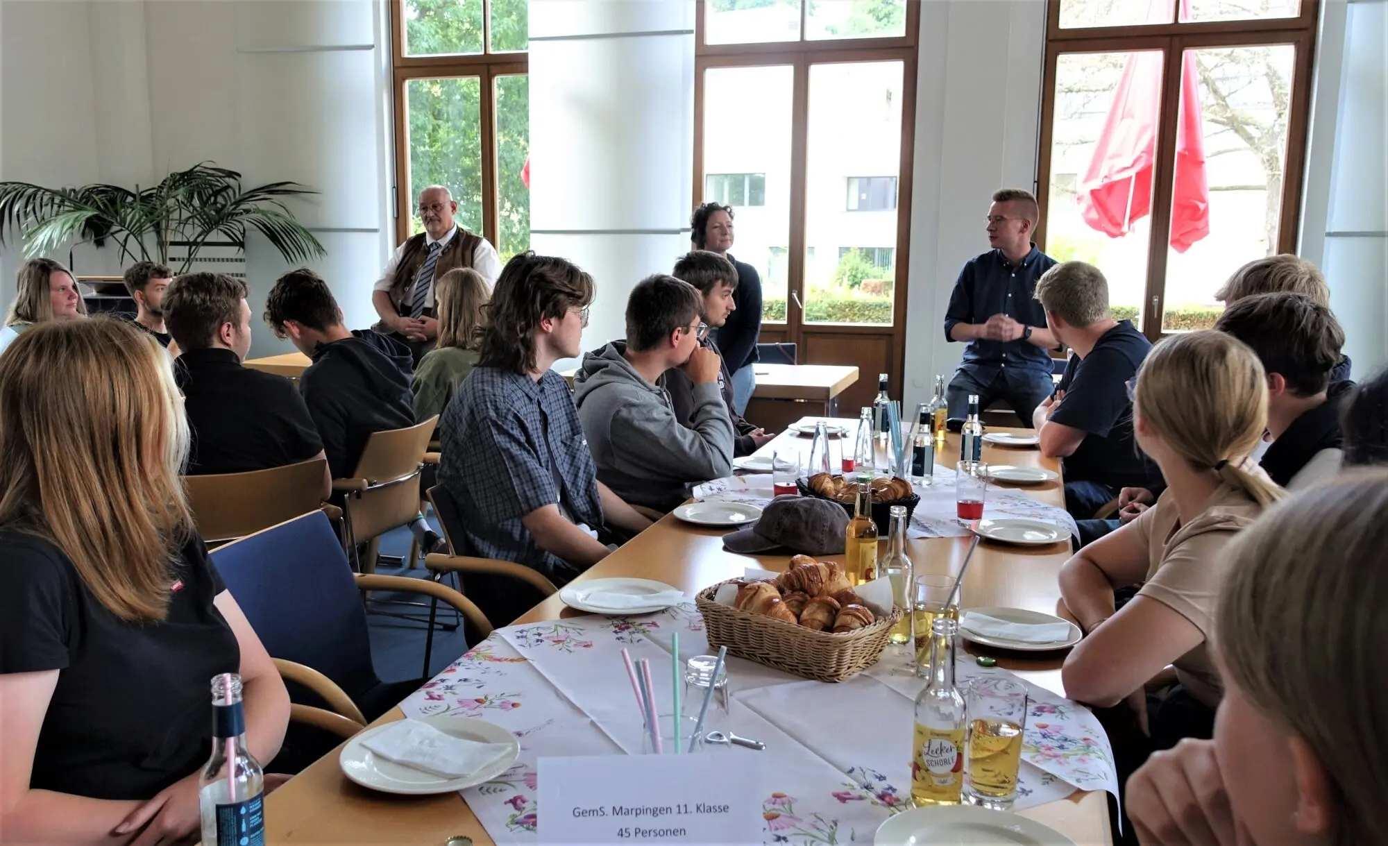 Jugendliche und Erwachsene an langen gedeckten Tischen bei einer Gesprächsrunde