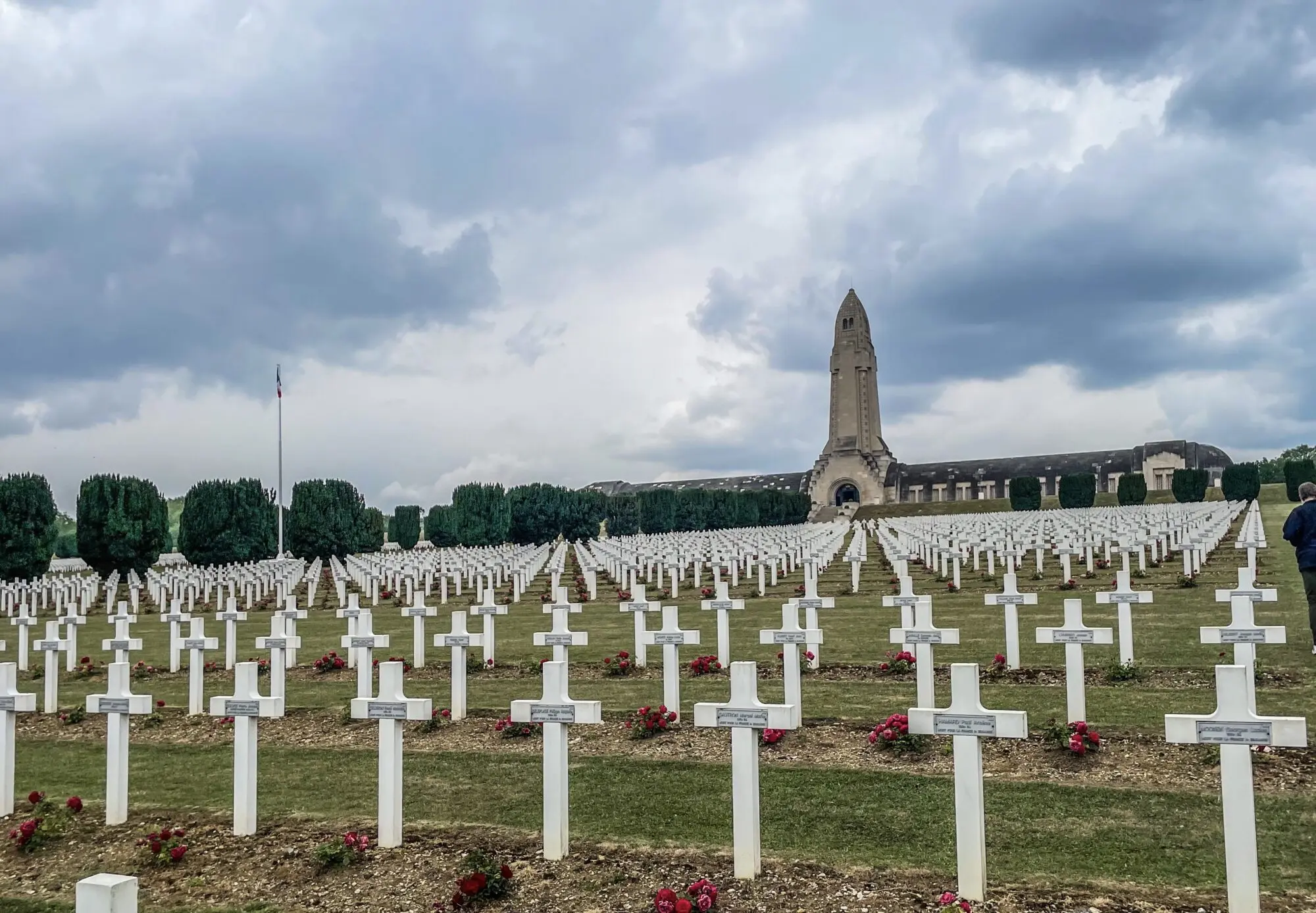 Soldatenfriedhof mit Reihen weißer Kreuze, im Hintergrund das Beinhaus mit hohem Turm unter bewölktem Himmel