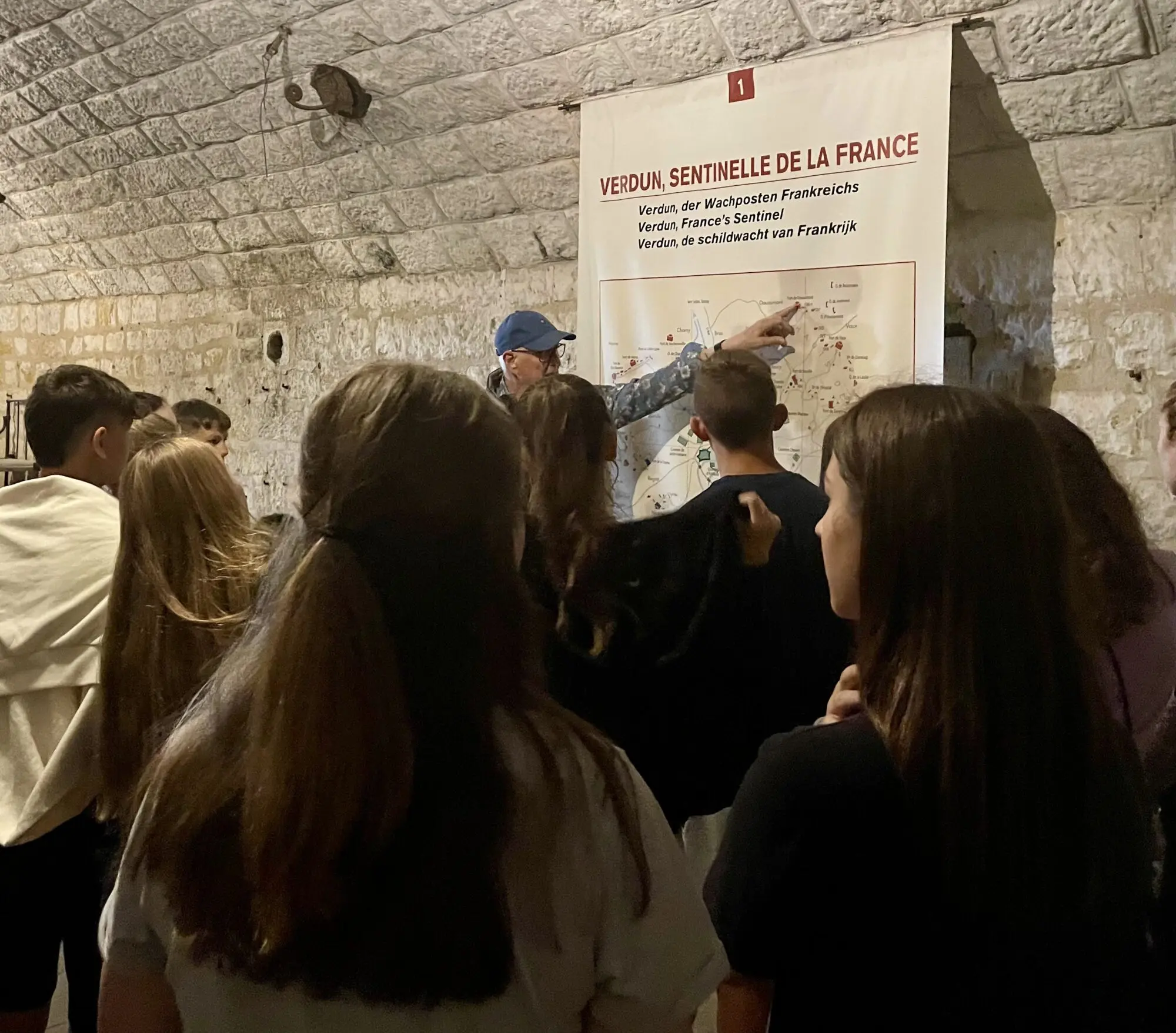 Schülerinnen und Schüler hören in einem unterirdischen Gang einer Festung einem Führer an einer Infotafel zu