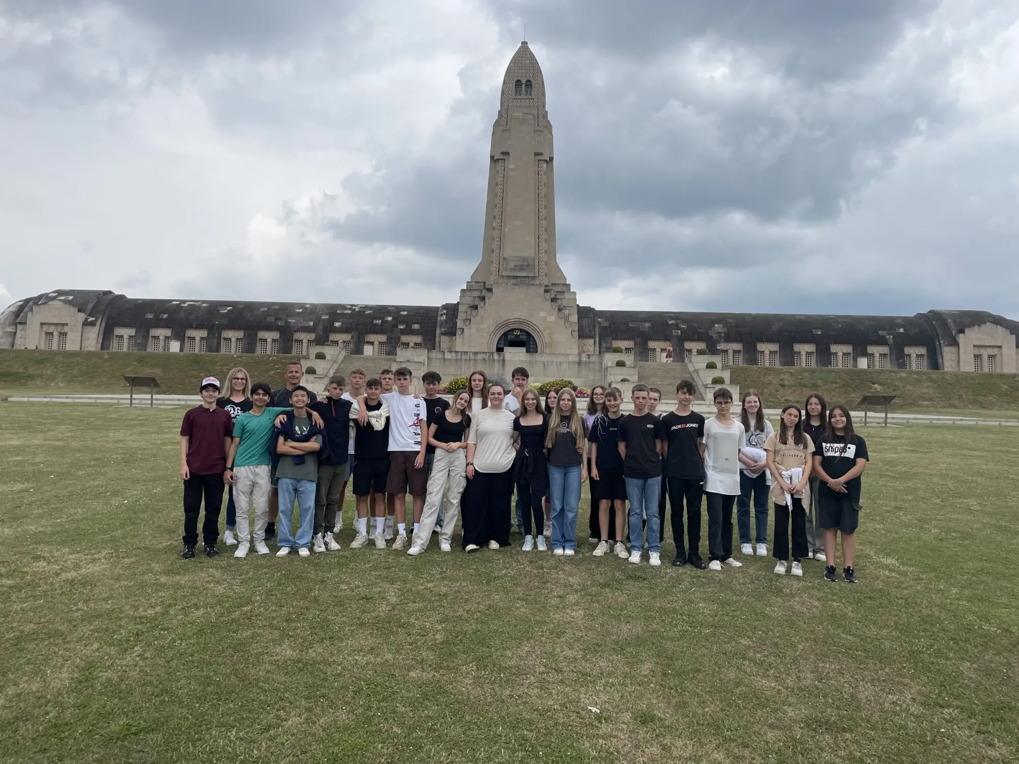 Gruppenbild der Klasse auf der Wiese vor dem langgestreckten Beinhaus mit Turm einer Kriegsgedenkstätte