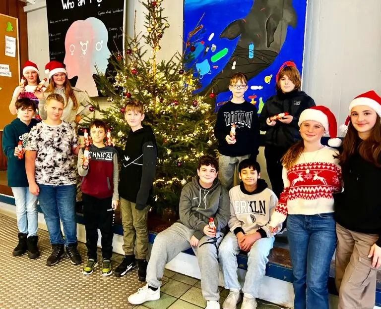 Schülerinnen und Schüler mit Weihnachtsmützen posieren vor einem geschmückten Weihnachtsbaum