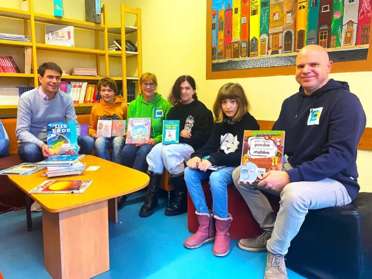 Kinder und zwei Erwachsene sitzen in einer Bibliothek und halten Bücher in den Händen