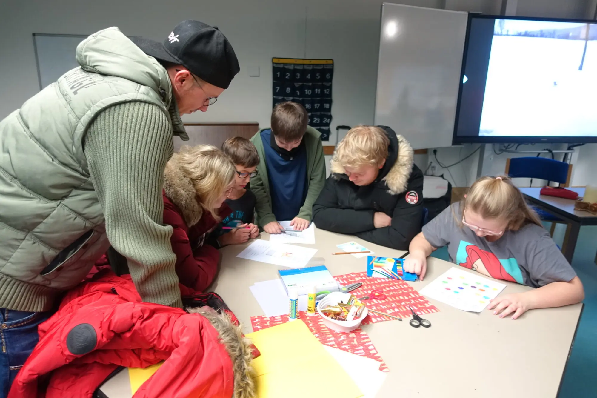 Kinder und Erwachsene sitzen an einem Tisch und arbeiten mit Papier und Stiften