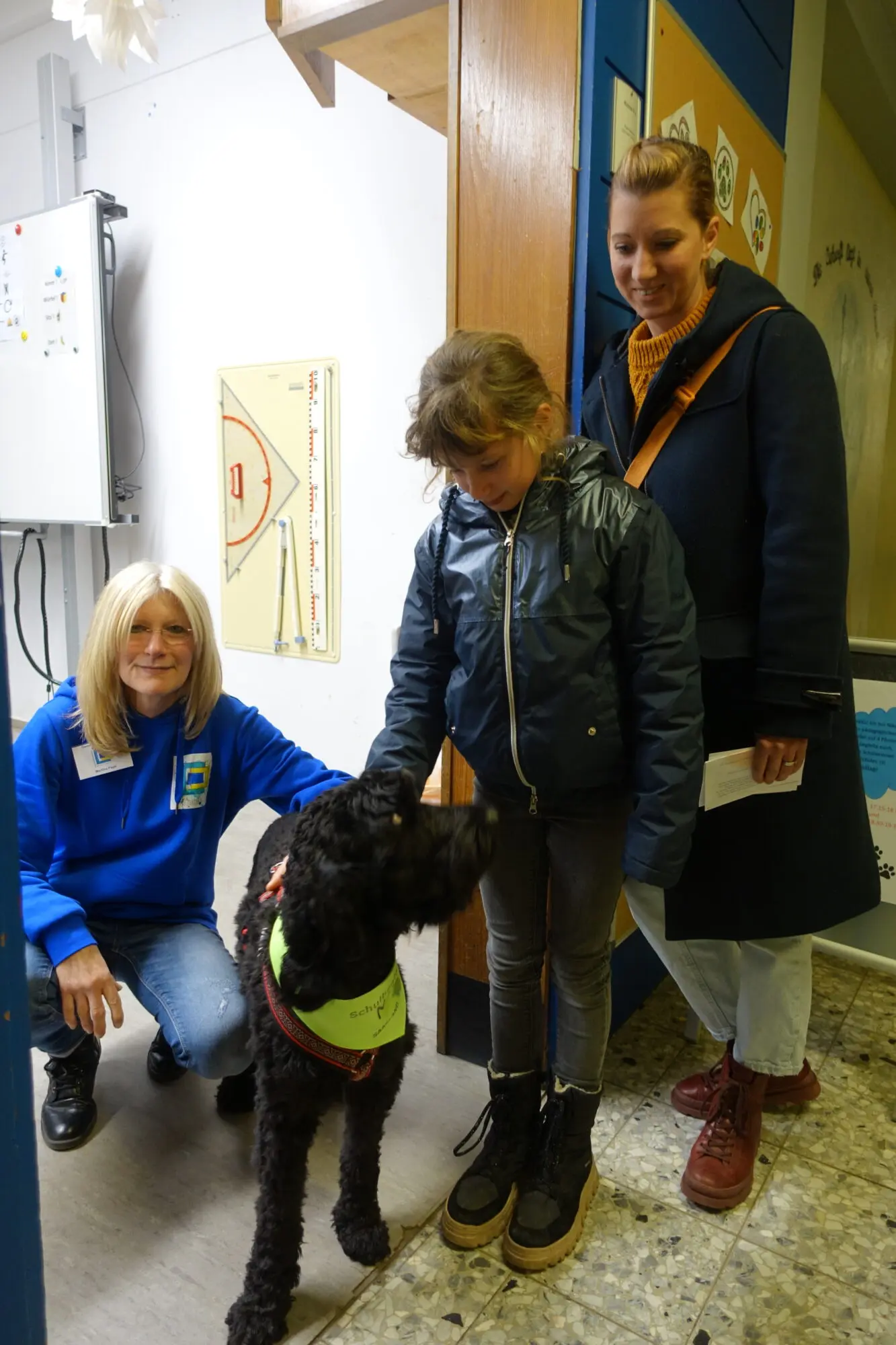 Kind und Erwachsene stehen im Flur, vor ihnen ein schwarzer Hund