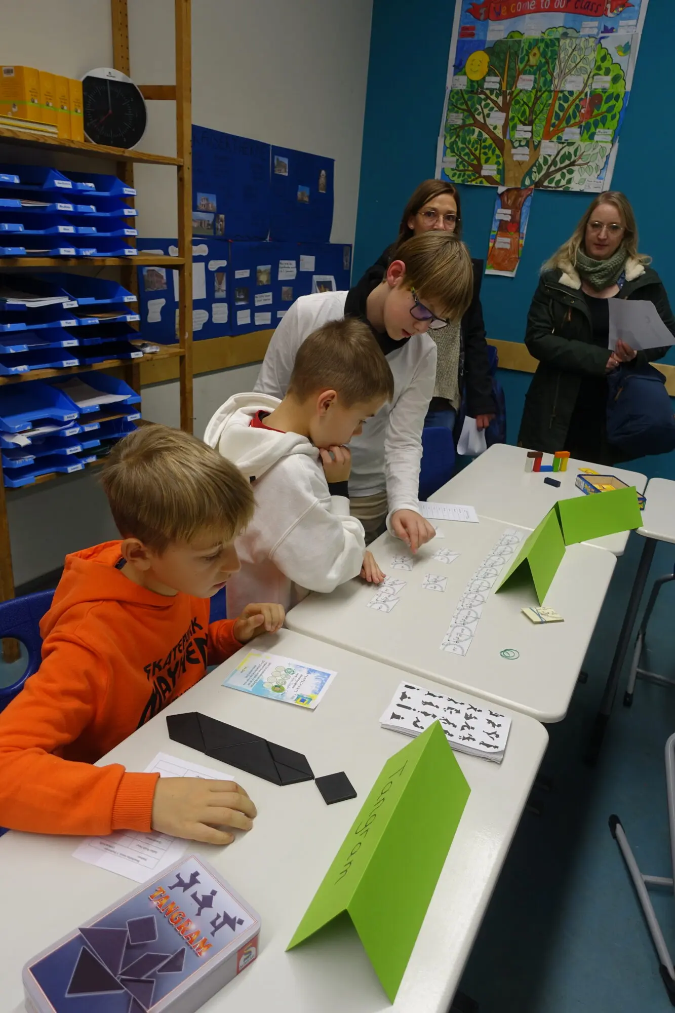 Kinder arbeiten an langen Tischen in einem Klassenraum mit Regalen