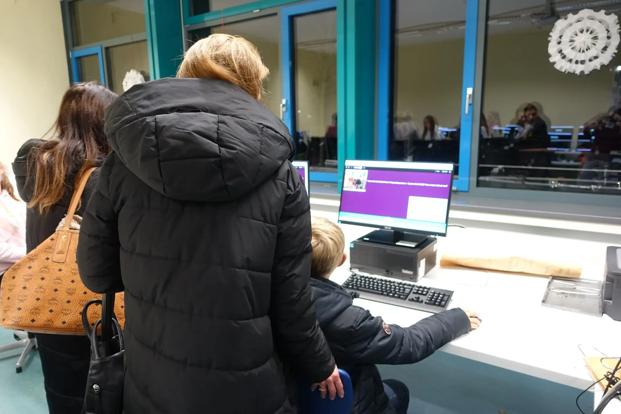 Eltern und Kind stehen an einem Computerarbeitsplatz und schauen auf den Bildschirm