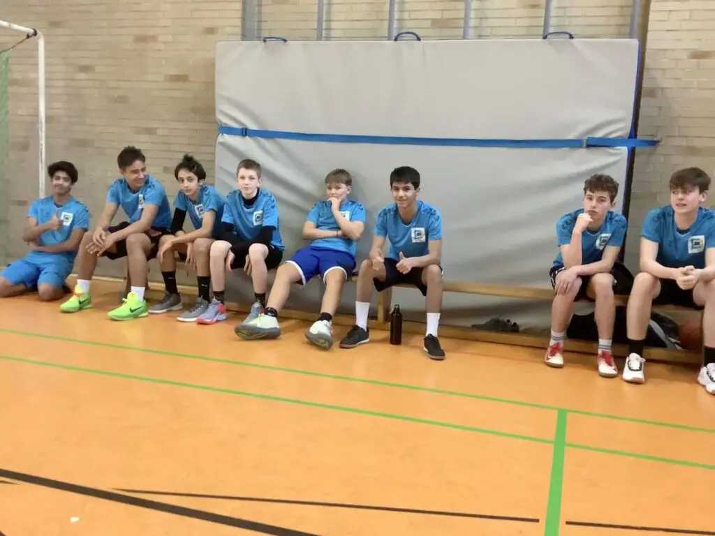 Schülermannschaft in blauen Trikots sitzt auf einer Bank in der Sporthalle